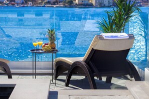 Un balcón con una silla de mimbre, una mesita con fruta y bebidas, y vista al mar.