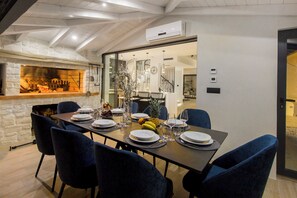 Ein Essbereich mit Steinwand, Kamin und einer durch eine Glastür einsehbarer, moderner Küche.