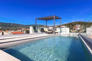 Ein Pool auf dem Dach mit Glasüberdachung, klarem blauen Wasser und Blick auf umliegende Gebäude und Hügel.