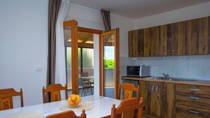 Zona pranzo con tavolo in marmo bianco, sedie in legno e una ciotola di frutta. Accanto, una cucina con mobili in legno e un forno a microonde.