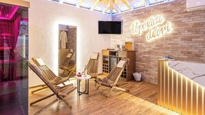 Ein Wellnessbereich mit Holzliegen, einer Rezeption und einer Ziegelwand mit einer Neonreklame.