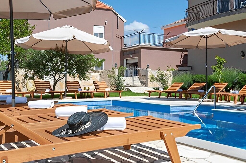 Ein Poolbereich mit Holzliegen, Sonnenschirmen und einem klaren, blauen Pool.