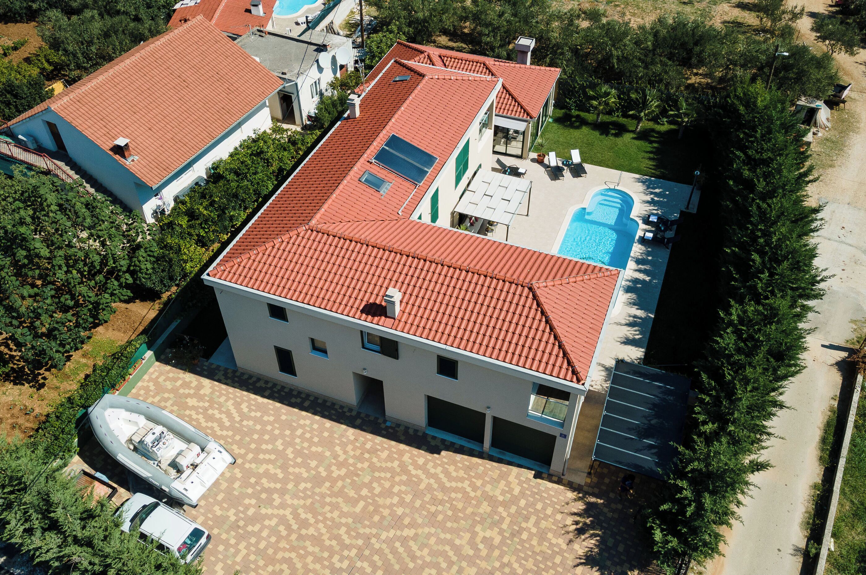 Une maison à deux étages, avec un toit recouvert de tuiles rouges, une piscine et un bateau amarré à l’extérieur.