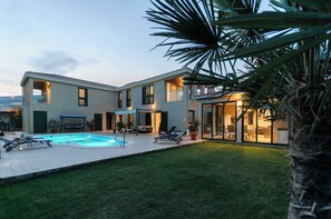 Ett modernt hus i två våningar med en swimmingpool, en uteplats och en välskött gräsmatta.