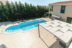 A swimming pool with a tiled deck, lounge chairs, and a covered area with tables. - Villa Jolanda (Trogir)