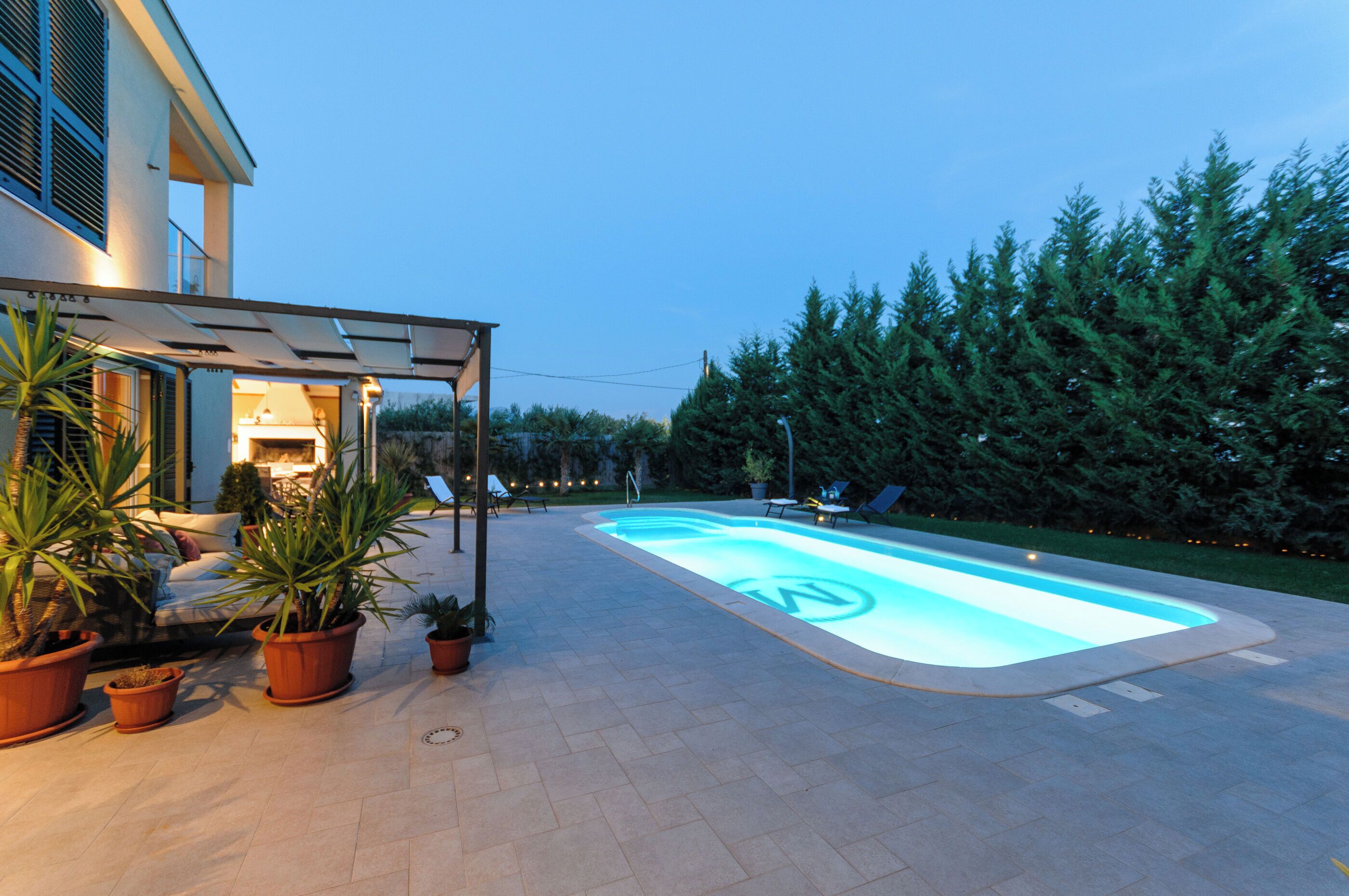 Une piscine au design géométrique, entourée de plantes en pot et de mobilier d’extérieur.