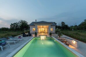 Een modern huis met een zwembad, zitplaatsen buiten en een goed verlicht terras.