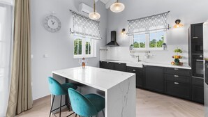Una cocina moderna con una isla de mármol blanco, gabinetes negros y taburetes de bar color turquesa.