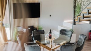 A modern living room with a glass-top dining table surrounded by cushioned chairs, a flat-screen TV mounted on the wall, and a staircase with a railing. - Villa The Rock (Vodice)