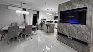 Una cocina moderna con televisor integrado, comedor con isla de mármol y zona de bar.