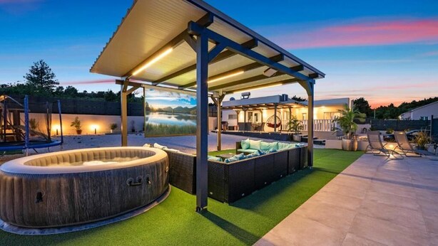 Un espacio al aire libre cubierto con un jacuzzi, asientos y vistas a un lago al anochecer.