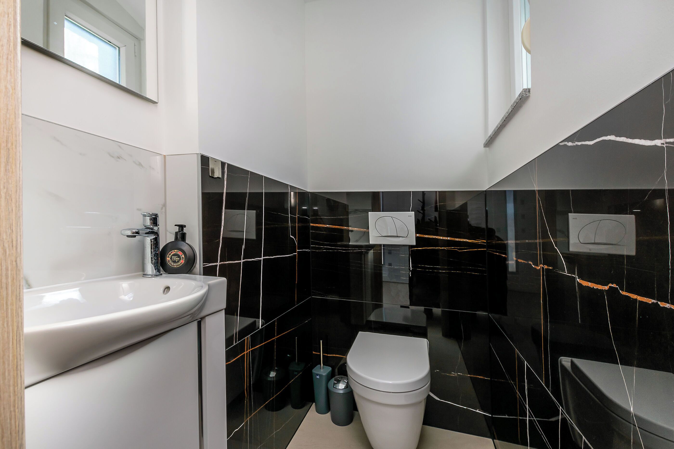 Un bagno moderno con un lavandino bianco, piastrelle di marmo nero, un water bianco e un piccolo cestino.