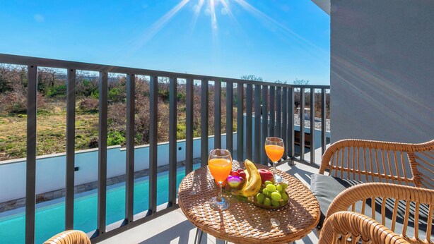A balcony with wicker furniture, a table with fruit and drinks, and a pool in the background. - Villa Klara (Policnik)