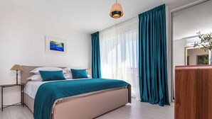 A bedroom with a bed, a bedside table, a lamp, a window with curtains, and a mirror. - Villa Klara (Policnik)