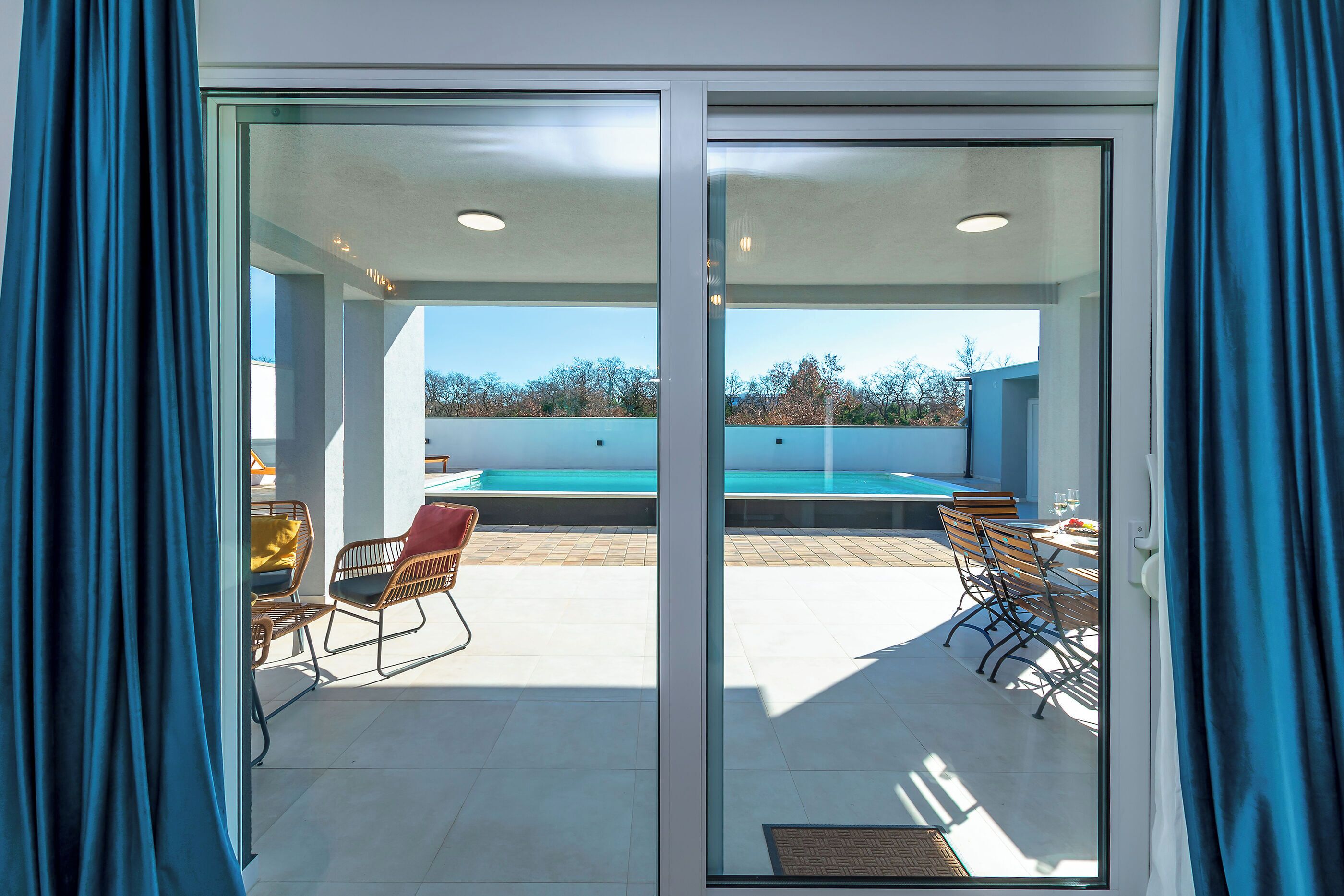 A modern room with a sliding glass door leading to an outdoor area with a pool, chairs, and a table.