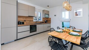 A modern kitchen with a wooden dining table, black chairs, and a hanging light fixture. - Villa Klara (Policnik)