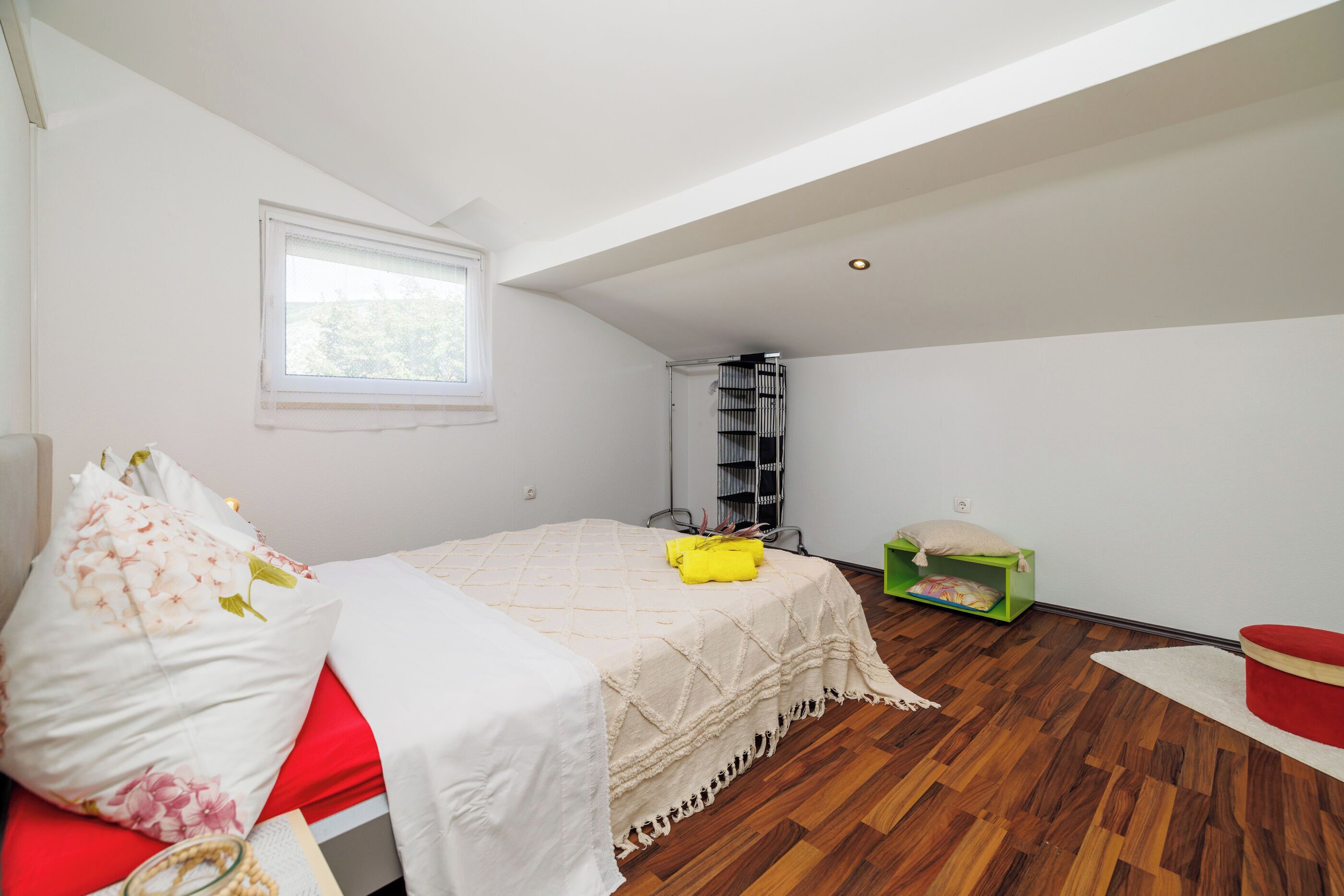A bedroom with a bed, a window, a green storage unit, and a red chair.