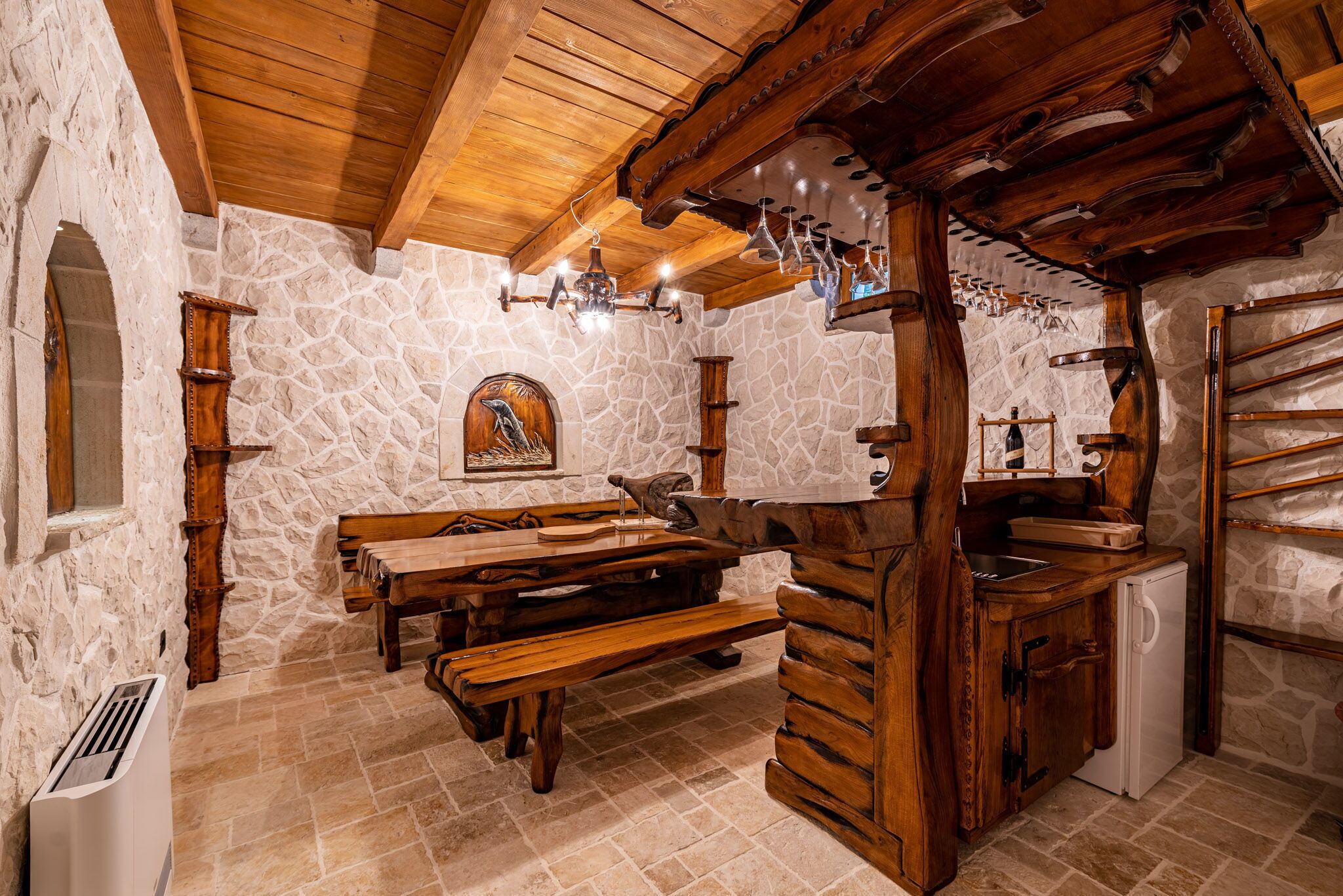 Una habitación rústica con paredes de piedra, bancos de madera, un mostrador de madera y una chimenea de piedra.