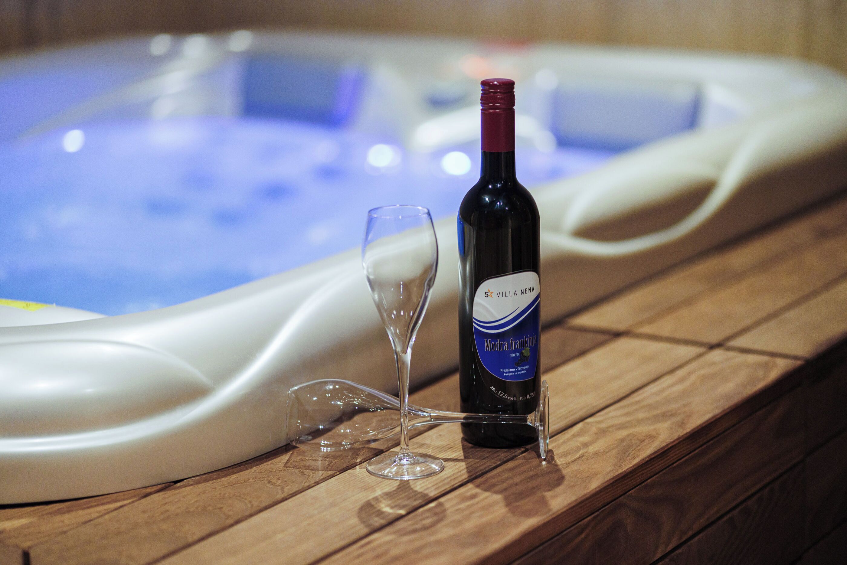 A bottle of wine and a glass on a wooden surface near a hot tub.
