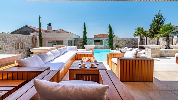 A poolside area with wooden furniture, a stone wall, and a clear view of the pool. - Villa Nena (Polaca)