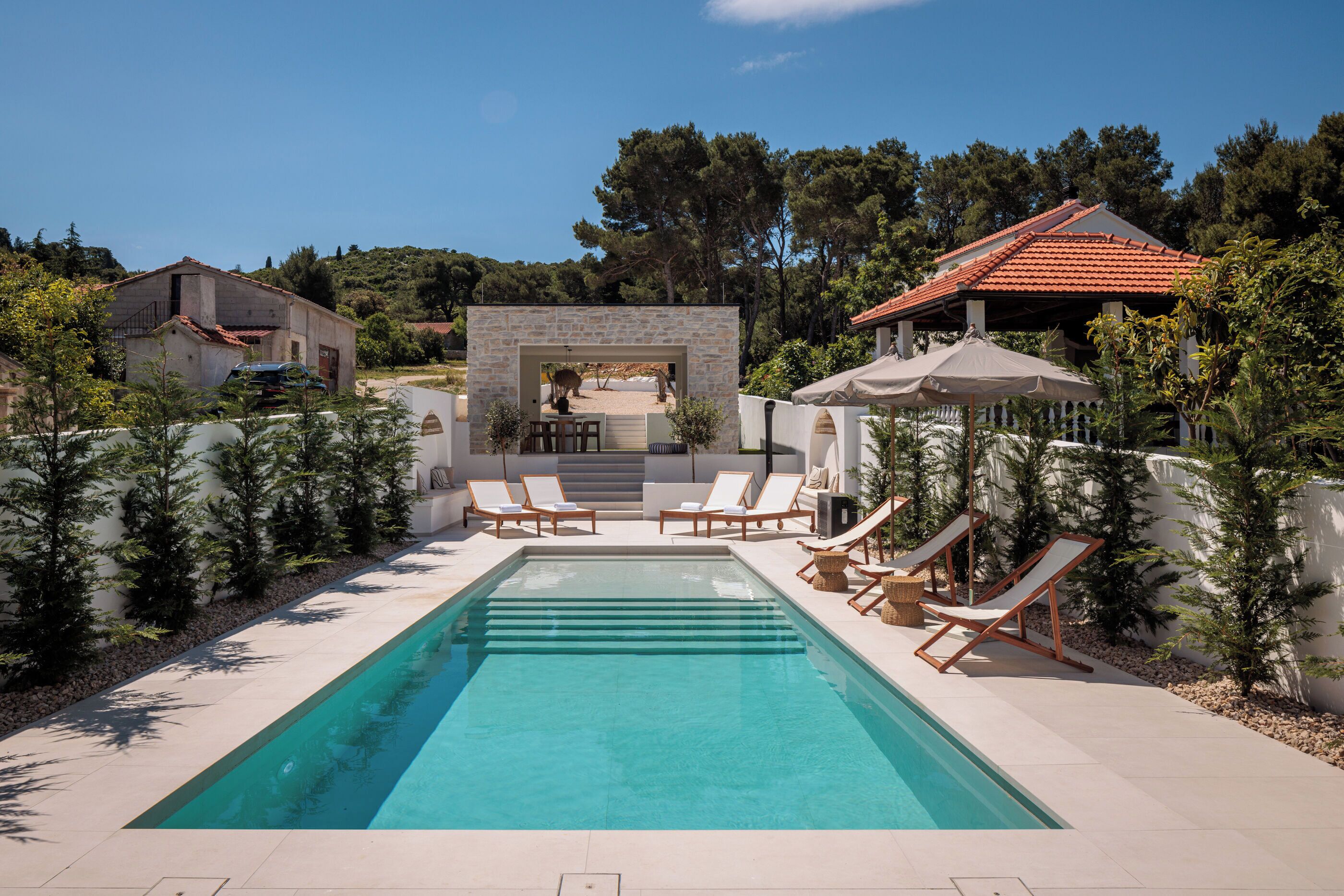 Une piscine rectangulaire, dotée de chaises longues, avec une structure en pierre en arrière-plan.