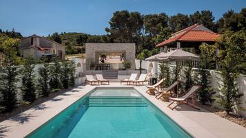 Une piscine rectangulaire, dotée de chaises longues, avec une structure en pierre en arrière-plan.