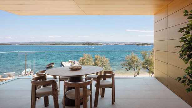 Un espace de restauration moderne avec une table ronde et des chaises, donnant sur une étendue d’eau où l’on peut apercevoir des bateaux et une côte lointaine.
