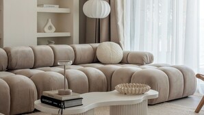 Un salon moderne avec un grand canapé d’angle, une console blanche et une bibliothèque agrémentée d’objets décoratifs.
