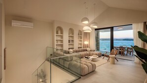 Un salon moderne avec un escalier en verre, un ensemble de canapés et une vue sur la mer.