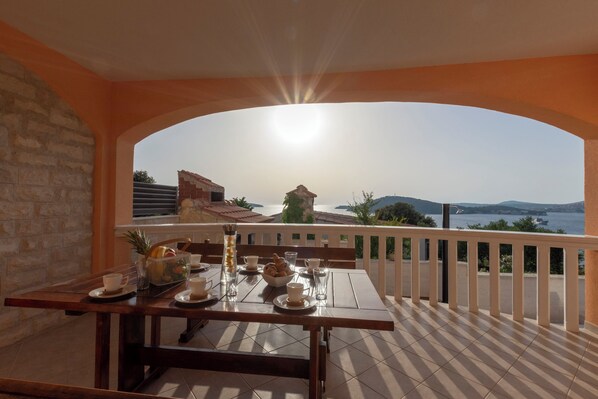 A dining area with a table set for two, overlooking a scenic view of the sea and hills. - Villa Patria (Rogoznica)