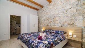 A bedroom with a stone wall, wooden beams, a bed with floral bedding, a bedside table with a lamp, and a wardrobe. - Villa Stone Castle (Vinodol)
