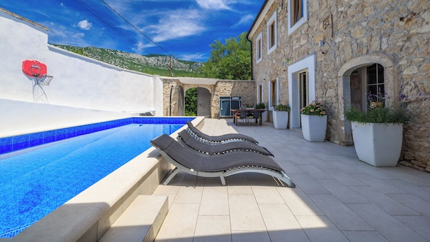 A swimming pool with lounge chairs, a stone building, and a mountain view. - Villa Stone Castle (Vinodol)