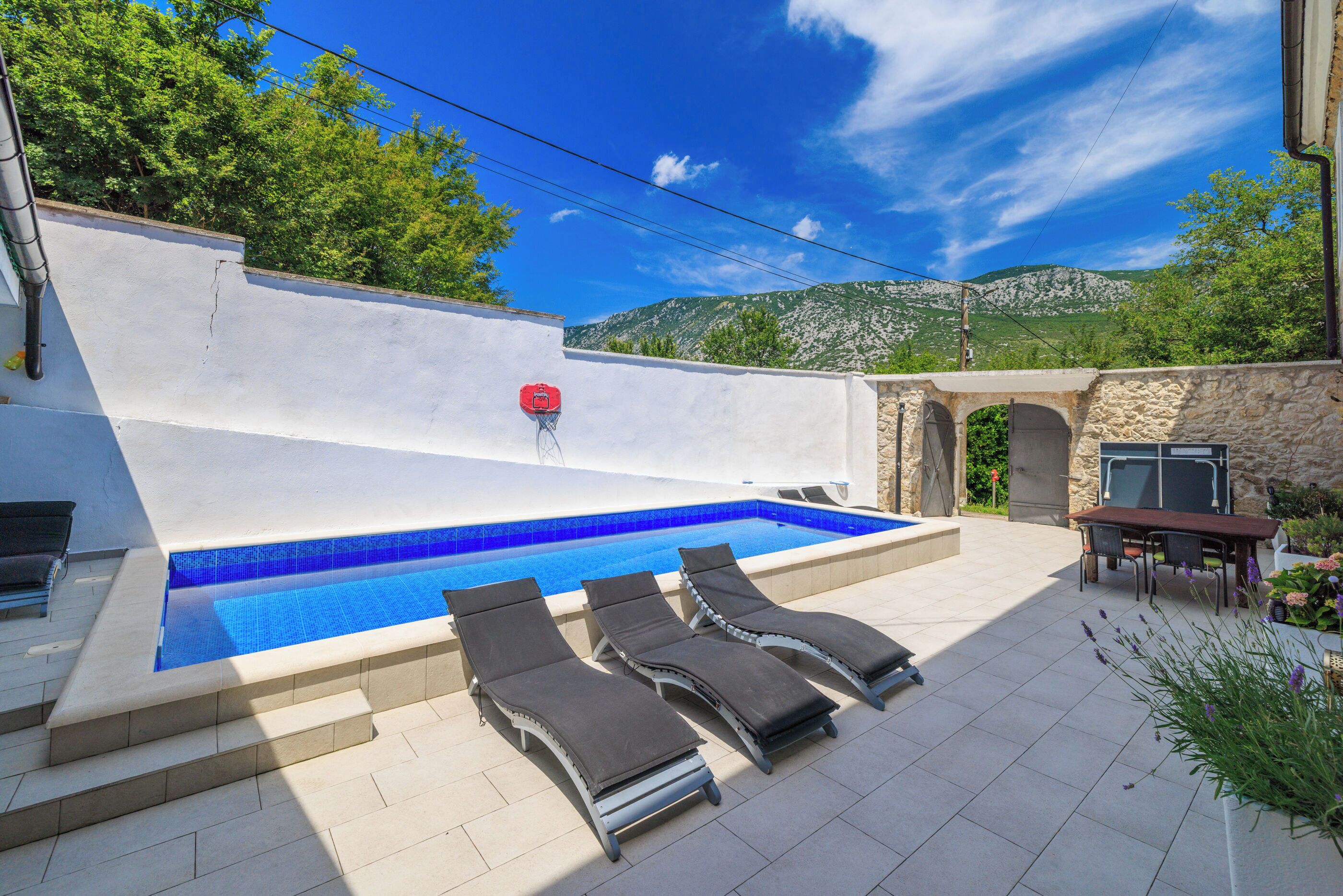 Una piscina con sillas de descanso, un muro de piedra y vistas a montañas.