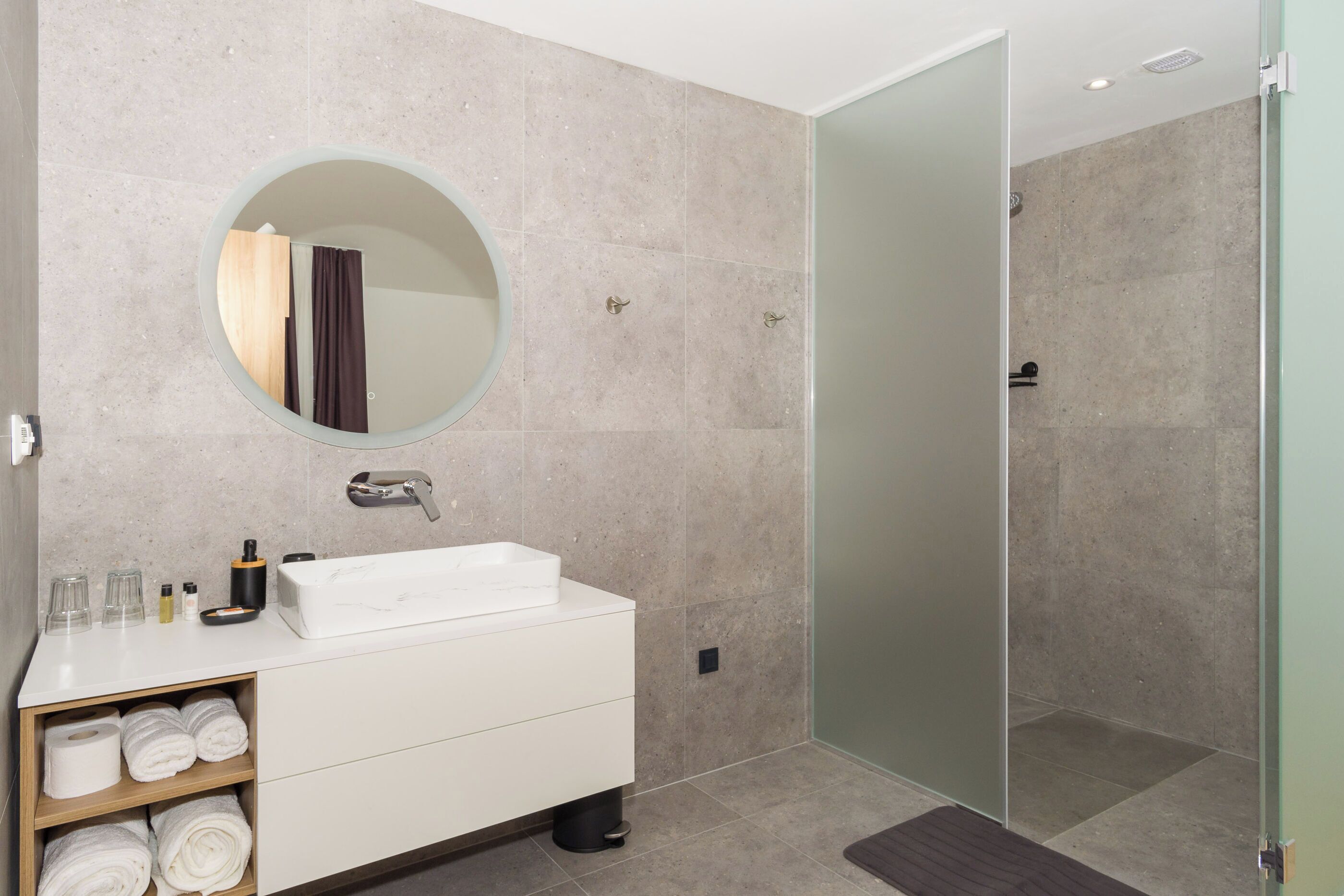 A modern bathroom with a round mirror, white sink, and a glass shower enclosure.