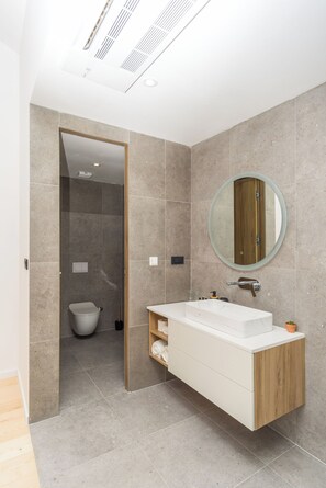 A modern bathroom with a built-in shower, a round mirror, and a wooden vanity. - Villa El Viento (Kraljevica)