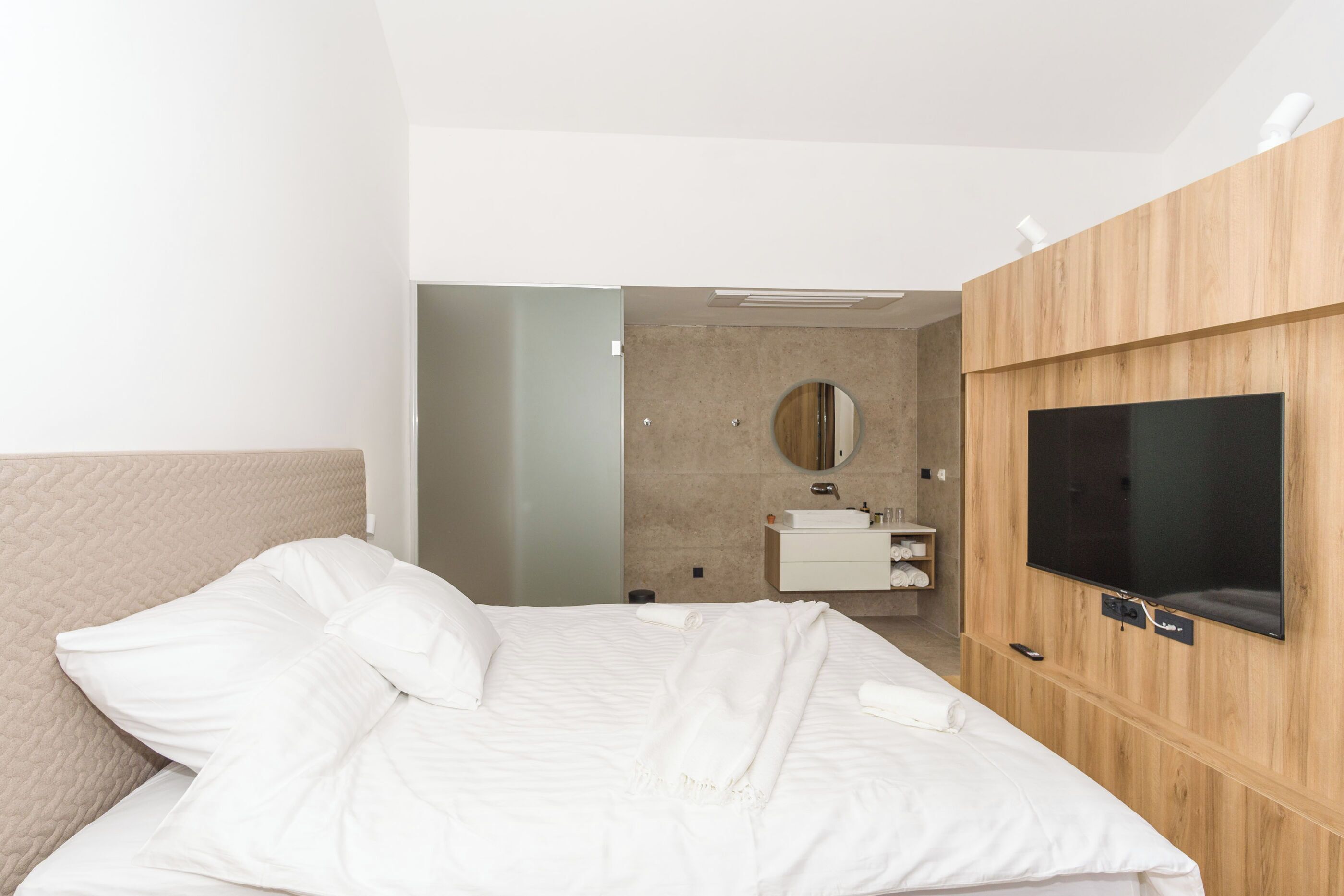 Habitación de hotel moderna con una cama grande, un panel de pared de madera, televisión y baño visible a través de una puerta abierta.