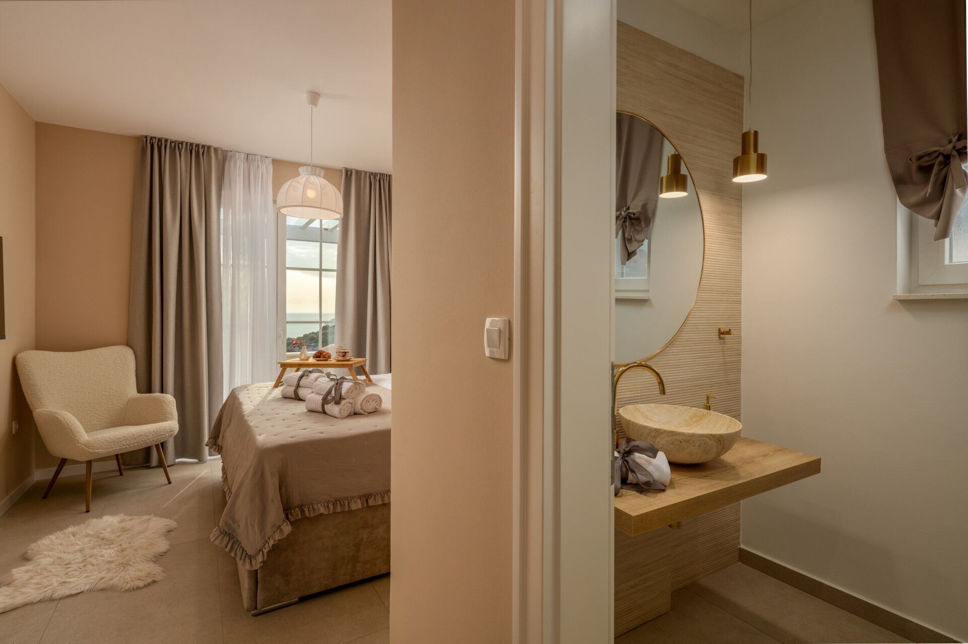 Ein Schlafzimmer mit Bett, Sessel, Nachttisch mit Lampe und Blick ins Freie durch ein Fenster.