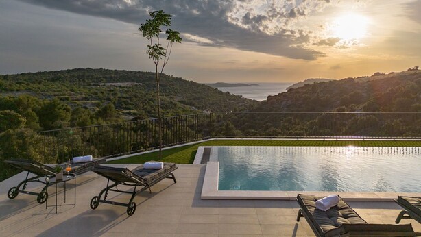 A swimming pool with lounge chairs and a small table, surrounded by a landscaped garden and a view of the sea. - Villa Gospoja (Rogoznica)