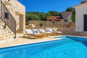A swimming pool with lounge chairs and a stone wall. - Villa Mare (Marina)