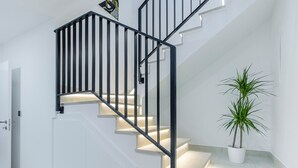 A modern staircase with black railings and illuminated steps, a potted plant, and white walls. - Villa Mare (Marina)