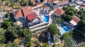 An aerial view of a residential area with stone buildings, a swimming pool, and surrounding greenery. - Villa Mare (Marina)
