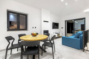 A modern living room with a round wooden table, black chairs, a blue sofa, and a flat-screen TV mounted on the wall. - Villa Mare (Marina)