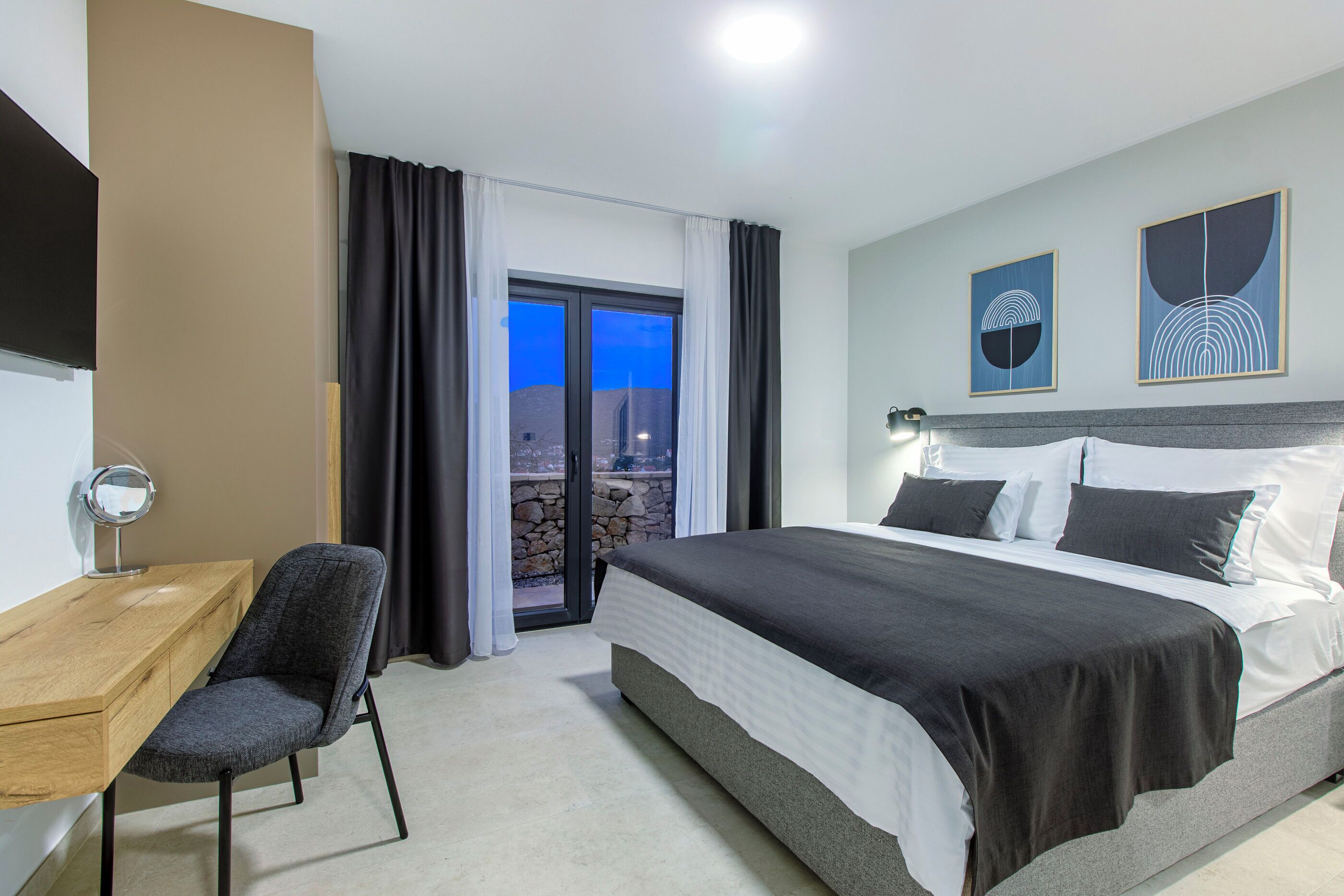 A hotel room with a bed, a desk, a chair, and a view through a glass door.