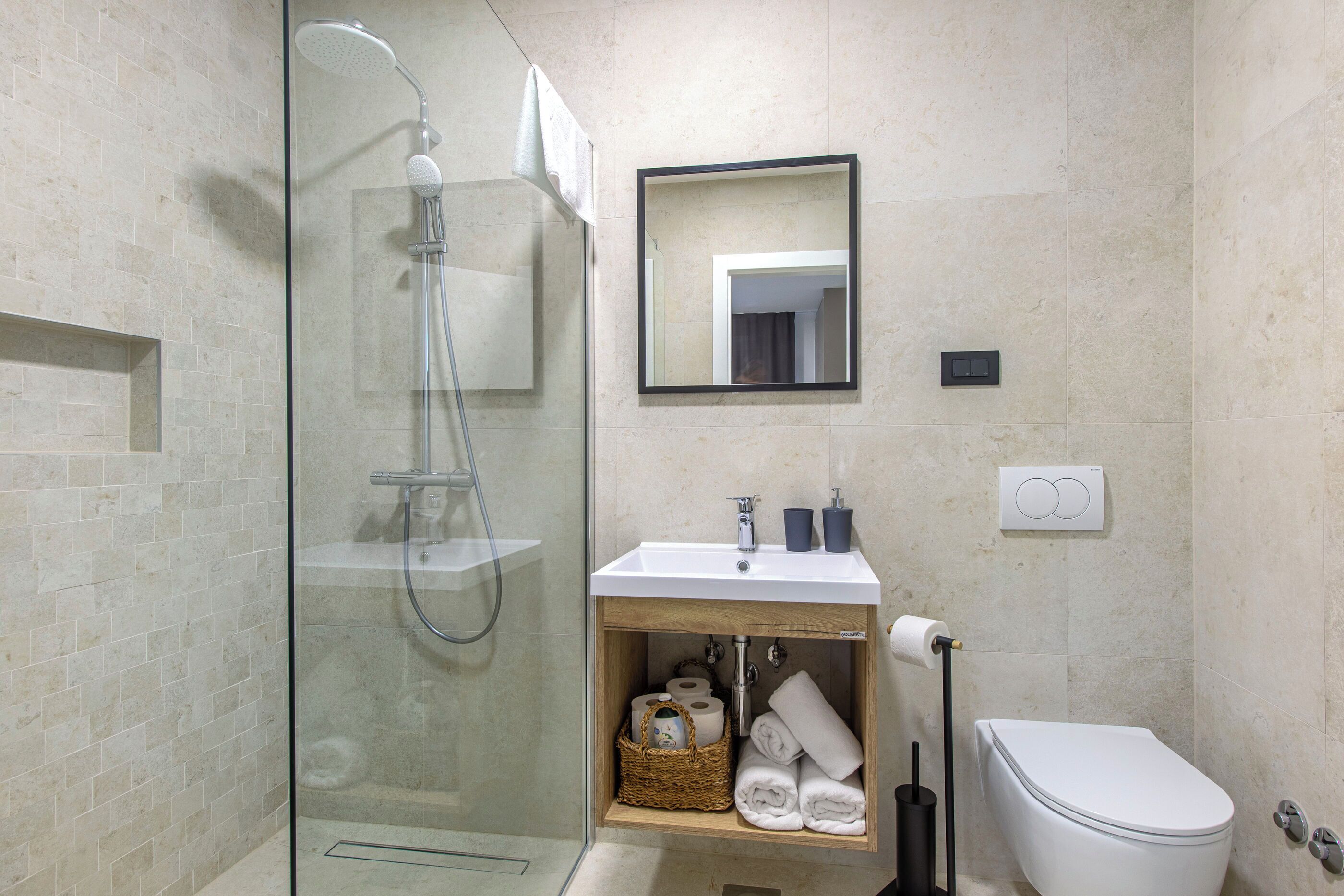 Un baño moderno con ducha envuelta en vidrio, un lavamanos blanco sobre un mueble de madera y un inodoro.