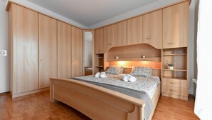 A bedroom with a bed, wooden wardrobe, and built-in shelving. - Villa Benedicta (Pakostane)
