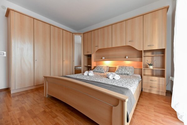 A bedroom with a bed, wooden wardrobe, and built-in shelving. - Villa Benedicta (Pakostane)