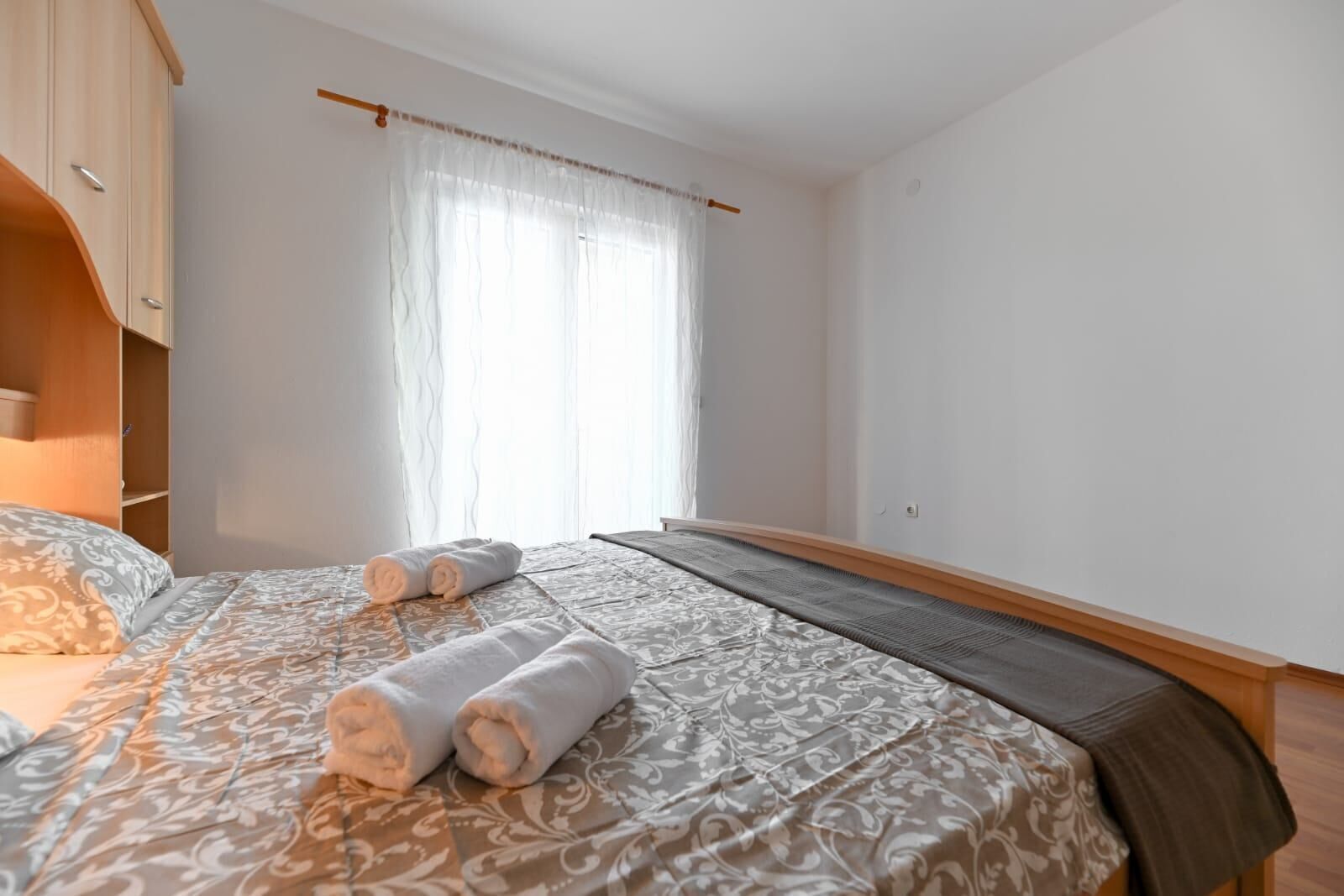 A bedroom with a bed, a wooden wardrobe, and a window with curtains.