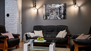 A modern living room with a black leather sofa, a glass coffee table with fruit, and a cityscape painting on the wall. - Villa Benedicta (Pakostane)