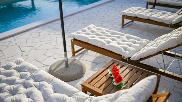 A poolside lounge area with cushioned chairs and a table with a glass dish of watermelon slices. - Villa Benedicta (Pakostane)