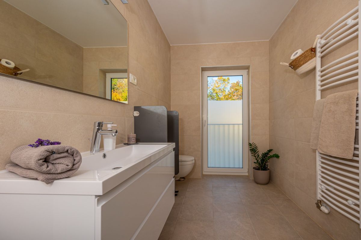 A modern bathroom with a white sink, a mirror, a towel, and a potted plant.
